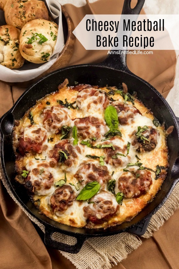 A skillet pan of cheesy meatballs on a brown background. A basket of knot rolls are seen in the back left.