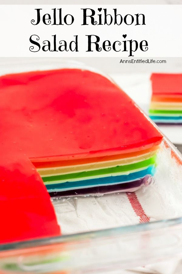 a cut out piece of jello ribbon salad on top of a stack of white dishes is in the background. The remainder of the ribbon salad in the pan is in forground