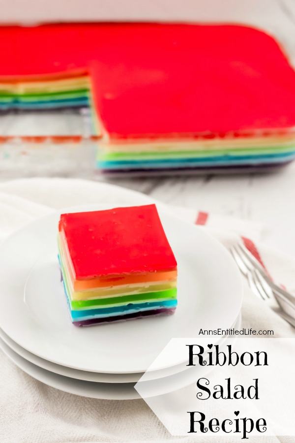 An overhead view of a cut out piece of jello ribbon salad on top of a stack of white dishes. The remainder of the ribbon salad in the pan is in the upper background