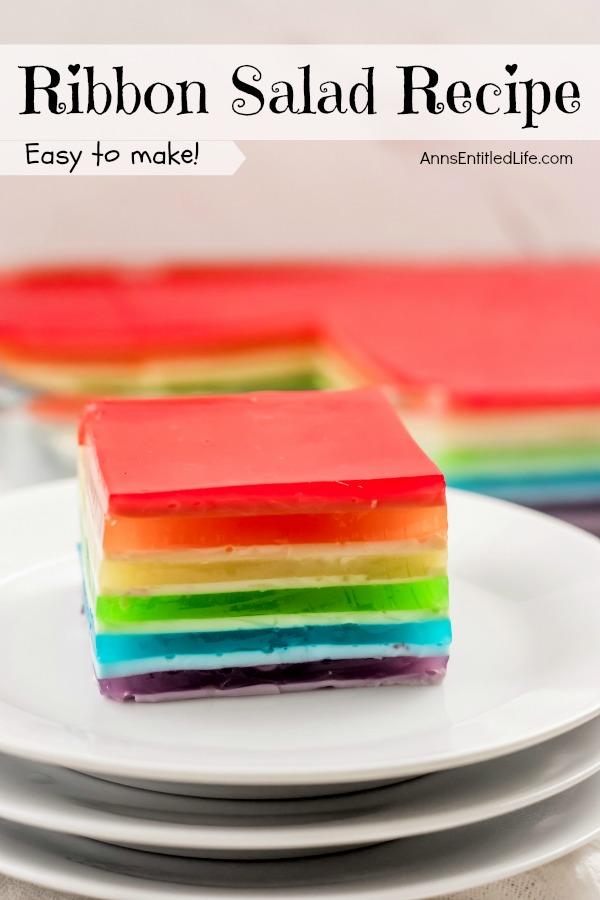 In the front, up close, is a cut out piece of jello ribbon salad on top of a stack of white dishes, a bit is missing from the jello ribbon salad. The remainder of the ribbon salad in the pan is in the upper background