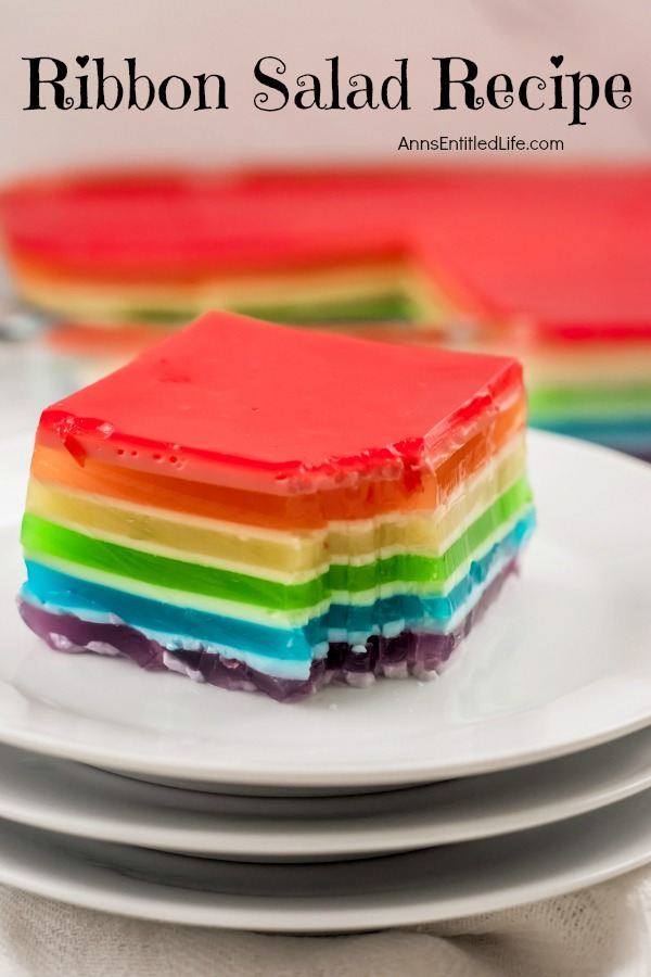 a cut out piece of jello ribbon salad on top of a stack of white dishes. The remainder of the ribbon salad in the pan is in the upper background