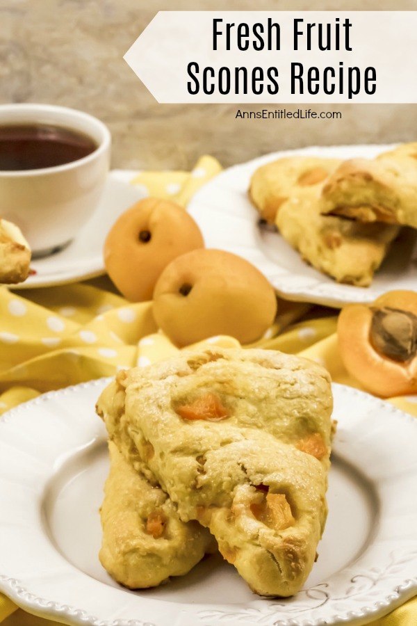 Two stacked apricot scones ona white plate. Two whole apricots are shown in the upper left, a cup of black coffee it higher on the left side, one fresh apricot cut in half is in the upper right. More stacked apricot fruit scones are in the far upper right.