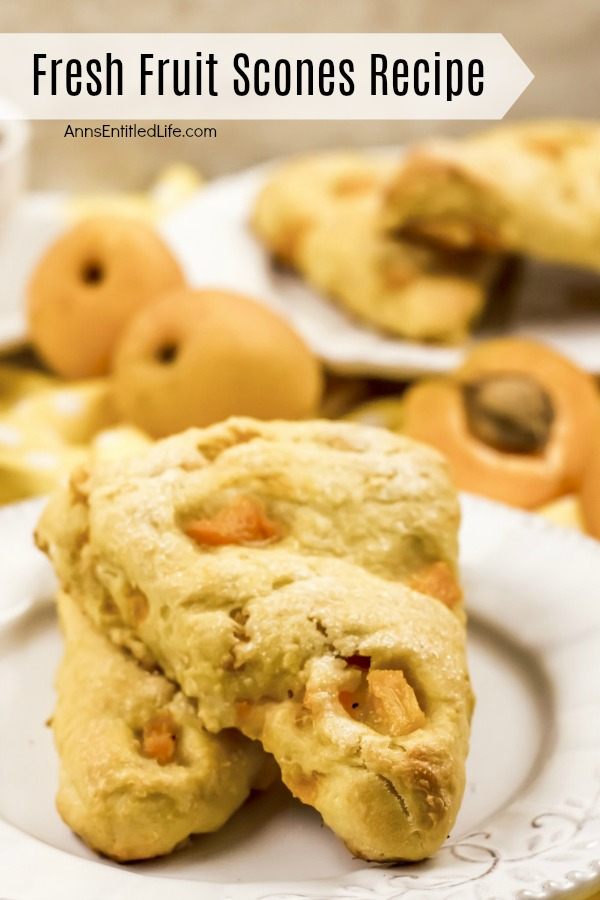 Two stacked apricot scones ona white plate. Two whole apricots are shown in the upper left, one fresh apricot cut in half is in the upper right. More stacked apricot fruit scones are in the far upper right.