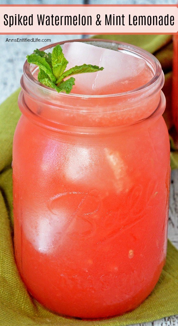 Close-up of a Mason jar glass filled with watermelon and mint lemonade on top of a moss green napkin set on a distressed blue board.