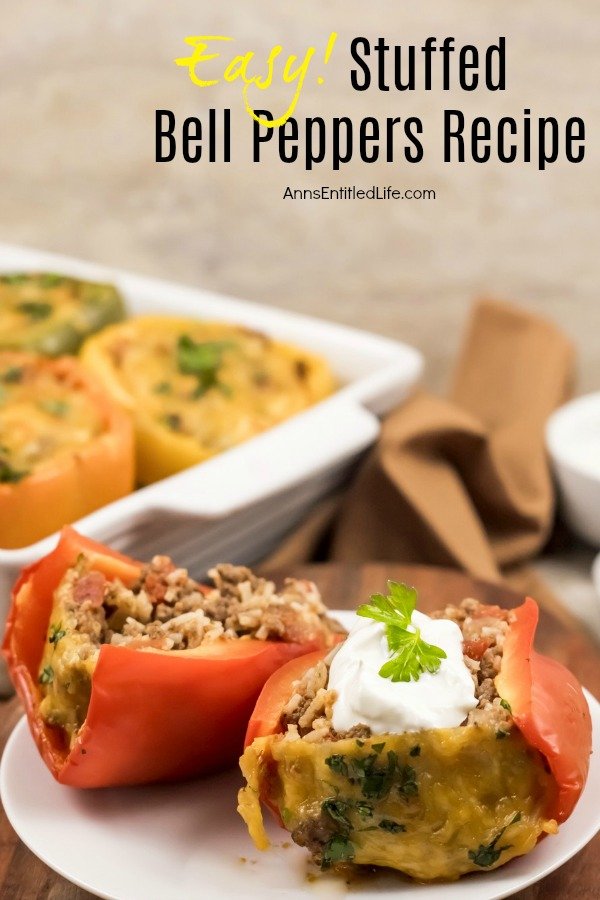 A close-up of a baked red pepper slit in half that is filled with a rice and beef mixture, in the upper right background is a white baking dish with three more baked bell peppers, all set atop a brown napkin