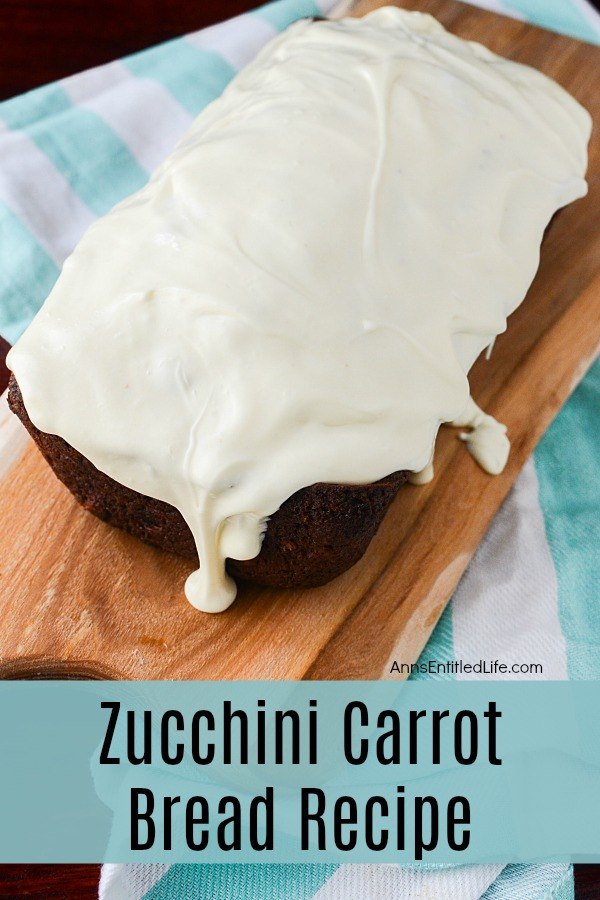 a full, cuncut loaf of frosted zucchini carrot bread on a butcher block cutting board, all atop of blue and white checked cloth