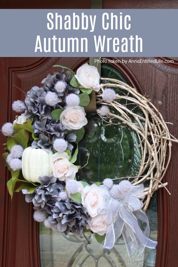 A beautiful fall wreath in colors of grey, blush, and white on a grapevine wreath, hanging on a brown door with a glass insert