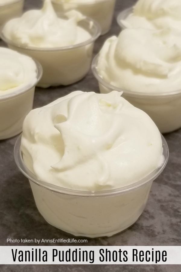 a vanilla pudding shot in a plastic soufflé cup at the forefront, 6 more pudding shots in the background, all on an aluminum pan