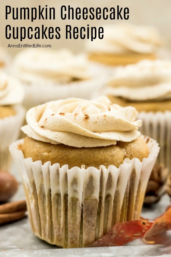 A close-up of a frosted pumpkin cheesecake cupcake sitting on an aluminum tray, a few faux fall foliage pieces are staged in front.