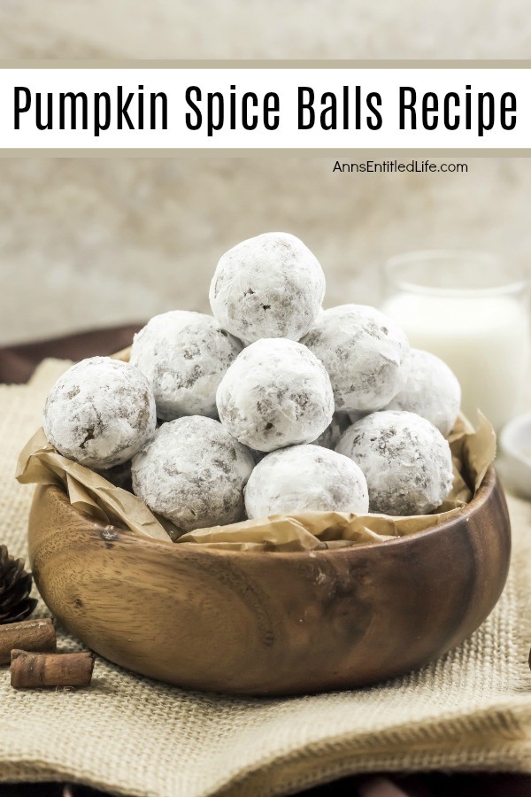 A wooden bowl filled with pumpkin spice balls is center, several pieces of cinnamon stick are to the bottom left, a glass of milk in the upper right. All set on a tan placemat, against a brownish background