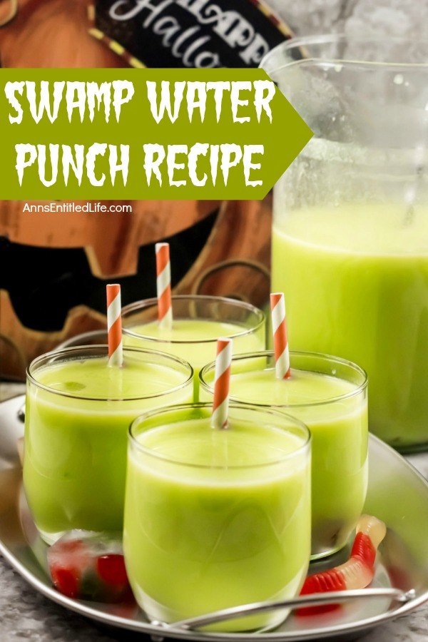 4 glass of green swamp water punch (with an inserted straw in each glass) on a galvanized tray. The remaining swamp water punch is in a pitcher to the right. A Halloween jack-o'-lantern sign is in the back. A few gummy worms are scattered about the tray.