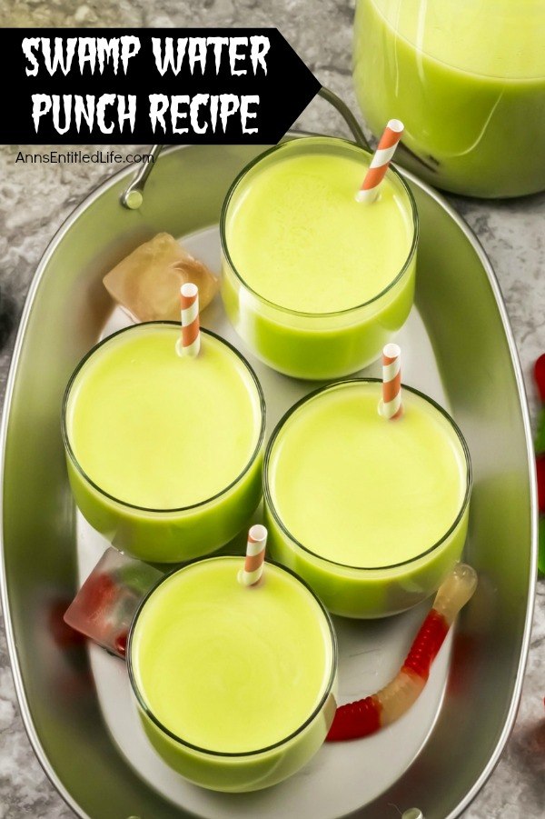 An overhead view of 4 glass of green swamp water punch (with an inserted straw in each glass) on a galvanized tray. The remaining swamp water punch is in a pitcher to the right. A few gummy worm ice cubes are scattered about the tray.