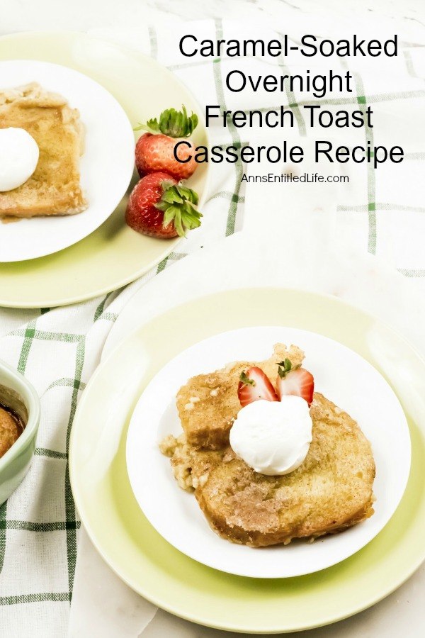 An overhead view of a serving of caramel-soaked French toast casserole on a white plate. There is a dollop of whipped cream on top, as well as a fresh strawberry. There is a second piece in the upper left, and in the upper right is a green and white checked dishcloth.