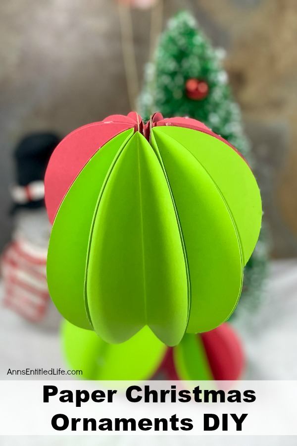 An upclose images of a green and red paper ornament. In the far background are two more smmall ornaments and a small faux evergreen tree.