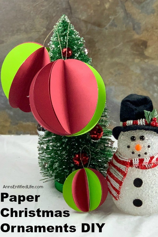 Three small green and red paper ornaments on a small evergreen tree. There is a faux snowman standing next to it.