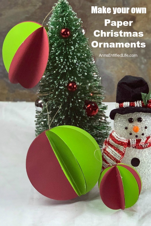 Three small green and red paper ornaments on a small evergreen tree. There is a faux snowman standing next to it.