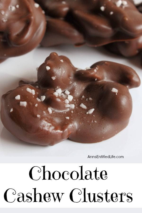 A homemade chocolate cashew cluster is front and center. A small pile of additional chocolates are in the background. These are set on a white paper.