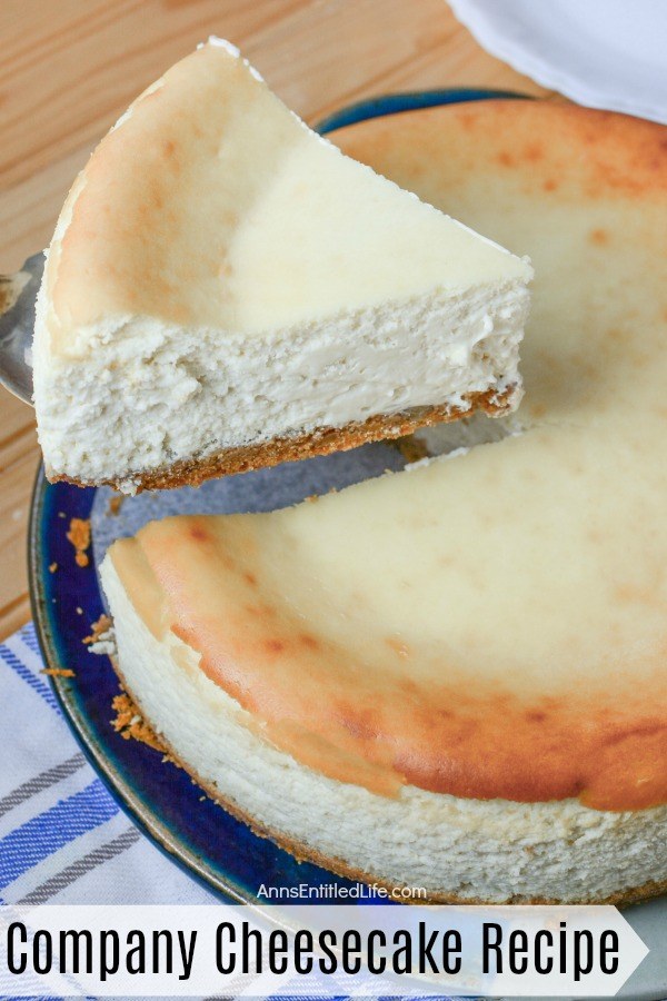 A side-view of a lifted piece of comapny cheesecake is on a pie lift. The remaining cheesecake is underneath on a blue earthenwear dish. This sits ontop of a blue and white dishtowel.