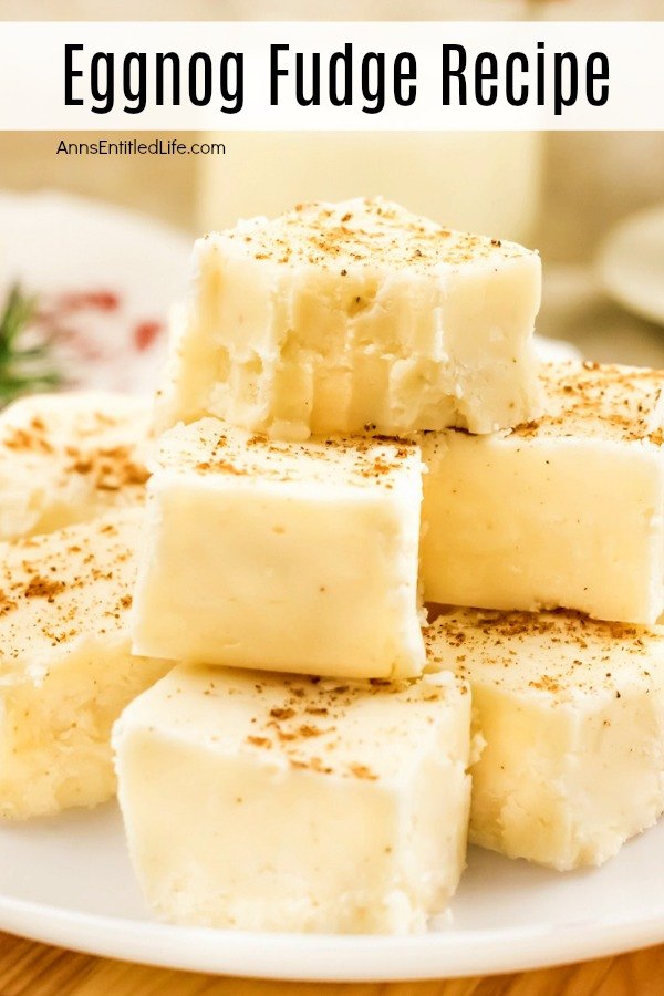 A close up of a white and red plate filled with cut pieces of eggnog fudge. There is a glass of eggnog directly above. They are sitting on a cutting board.
