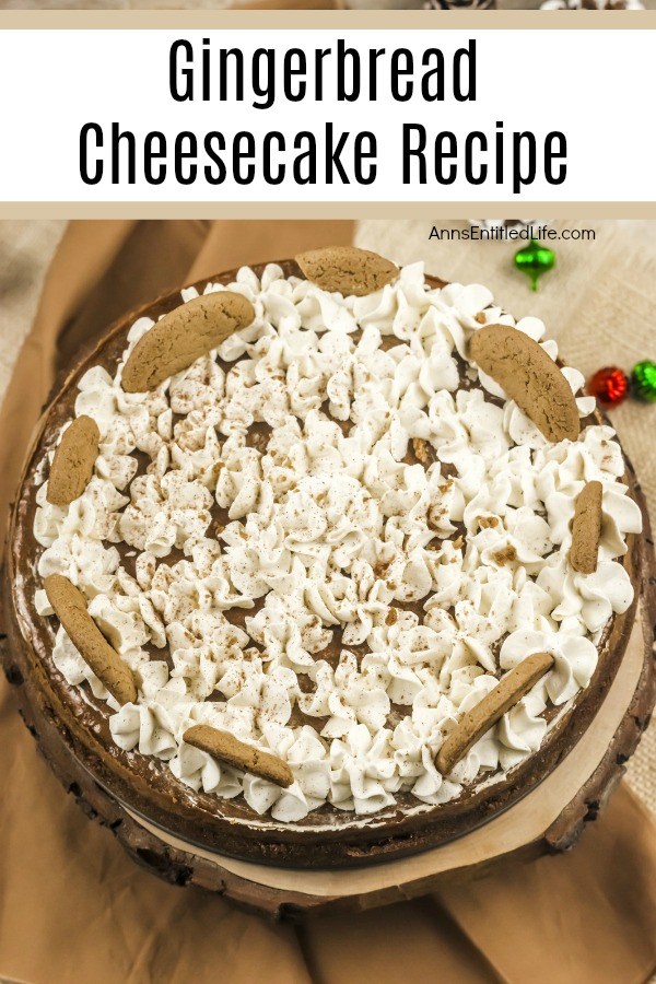 A whole gingerbread cheesecake sitting on a wooden serving tray on top of a brown countertop. The cheesecake is decorated with whipped cream and gingersnap cookies.