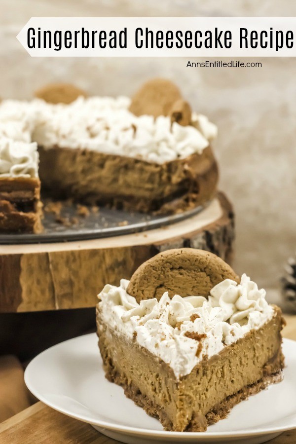 A front profiled slice of gingerbread cheesecake sits on a white plate. The rest of the cheesecake sits on top of a wooden serving tray in the upper left of the photo.