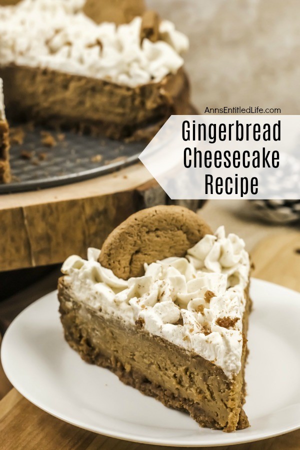 A piece of pie that is side-profiled of gingerbread cheesecake sits on a white plate. The rest of the cheesecake sits on top of a wooden serving tray in the upper left of the photo.