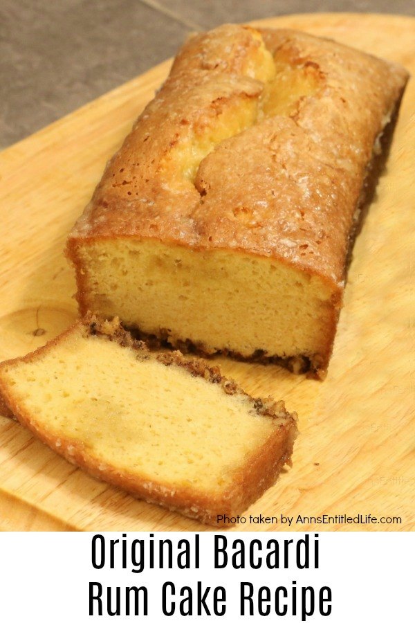 Bacardi rum cake baked in the shape of a loaf sits on a wood cutting board. The end of the rum cake is sliced to show the inside of the rum cake.