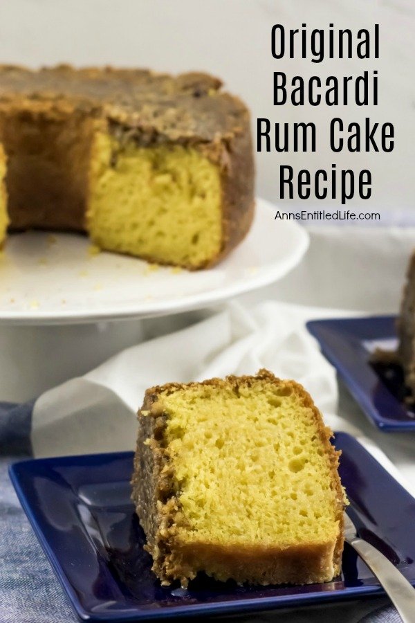 A cut Bacardi rum cake on a white cake server. A piece of rum cake is served on a blue plate in the front center. This is all on top of a white and blue bloth.