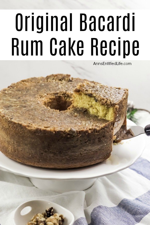  Bacardi rum cake on a white cake server. A piece of rum cake is being lifted using a cake server. There is a bowl of nuts in the center front. This is all on top of a white and blue cloth.