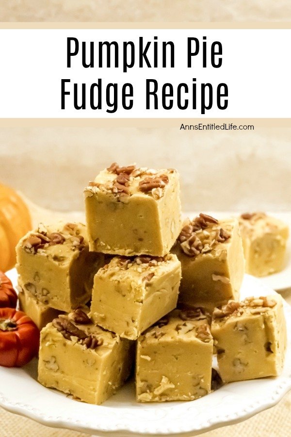 A stack of cut pumpkin pie fudge sitting on on a white plate is front and center. Several decorative faux orange pumpkins are sitting on the left side of the plate.