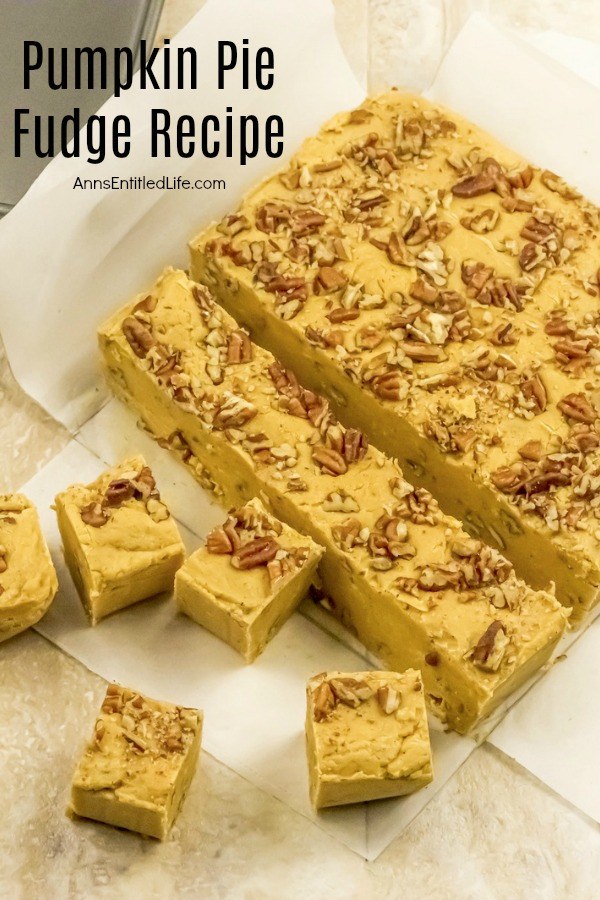 A slab of pumpkin pie fudge sitting on parchment paper on a cutting board. Several slices and squares are cut.