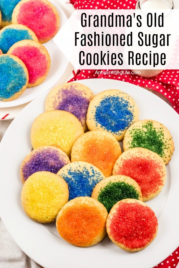 A white plate filled with homemade sugar cookies with various sugar tops, there is a second plate in the upper left. These sit on top of a red polka dot napkin.