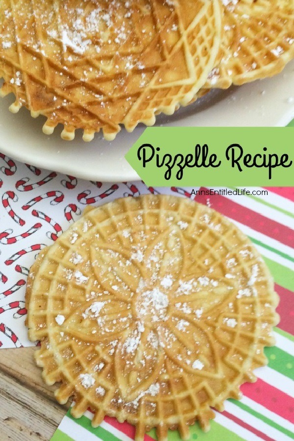 A white plate filled with pizzelles which are covered in powder sugar is in the upper portion of this photo. A lone pizzelle sits front and center on a striped holiday paper.