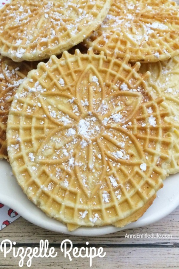 An upclose view of a white plate filled with pizzelles which are covered in powder sugar.