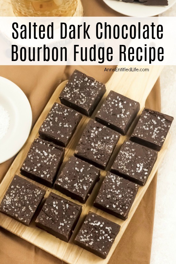 An overhead view of 12 square pieces of salted dark chocolate bourbon fudge on a wooden cutting board which is set upon a gold napkin. There are three plates surrounding the cutting board on the outer edges of the image.