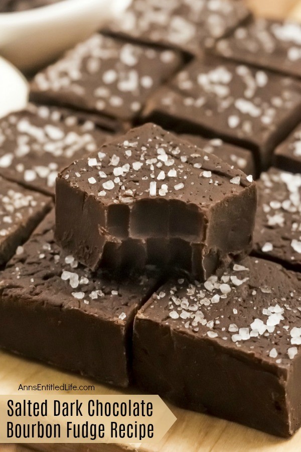 An up-close image of 12 square pieces of salted dark chocolate bourbon fudge on a wooden cutting board. The top piece has a bite removed so you can see the inside of the fudge.