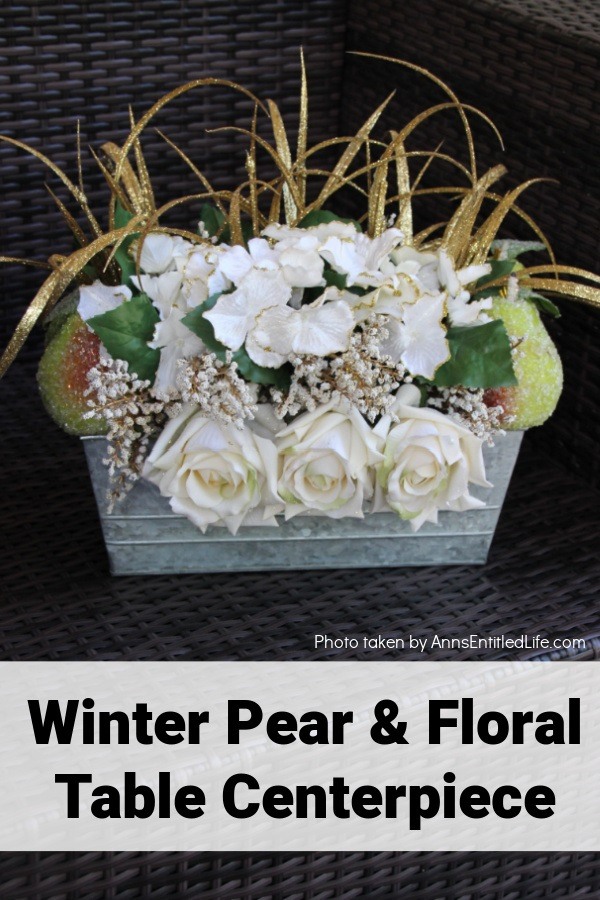 A rectangular galvanized tin filled with faux white floral, pears, and tall gold grass on a brown wicker chair