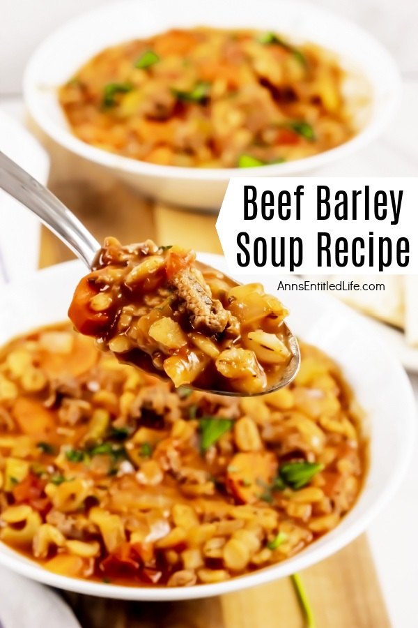 A spoon filled with beef barley soup is being lifted from the white soup filled bowl below it, a second bowl is in the upper part of the image. The bowls sit on a wooden board.