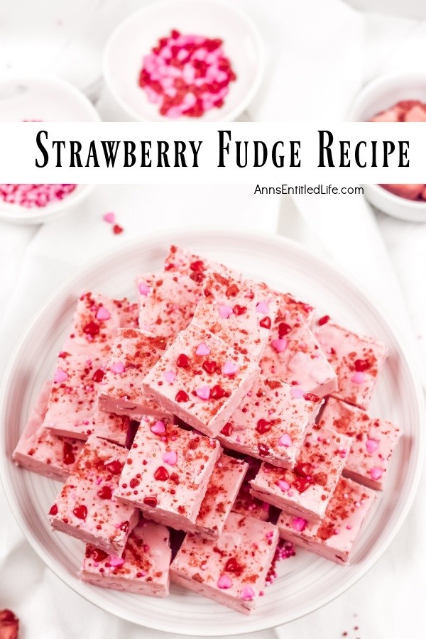 An overhead view of strawberry fudge squares stacked in a pyramid shape on a white plate. There are small bowls of red sprinkles that surround the plate.