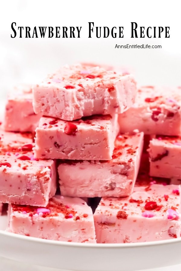 Strawberry fudge squares stacked in a pyramid shape on a white plate, the top piece has a bite removed