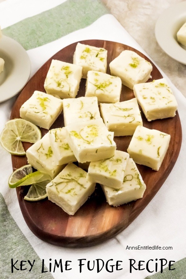 An overhead view of a wooden tray filled with cut squares of key lime fudge, garnished with limes. In the background are white bowls filled with more fudge