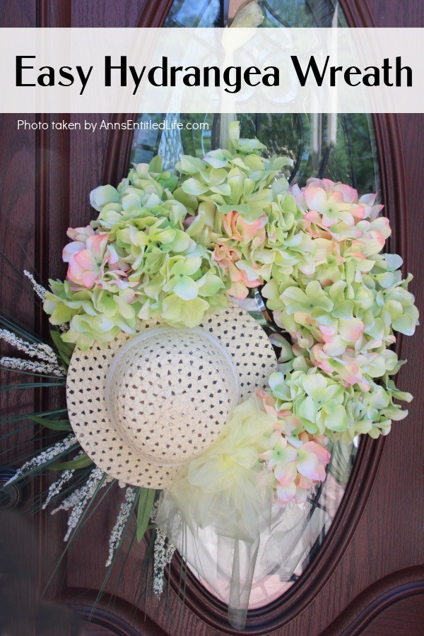 Up close photo of a Hydrangea Wreath made with a hat, hanging off a door hanger against a brown door with a glass window.