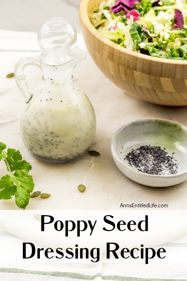 A cruet filled with poppy seed dressing, a bowl with poppy seeds to the lower right, a partial view of a salad in the upper right side