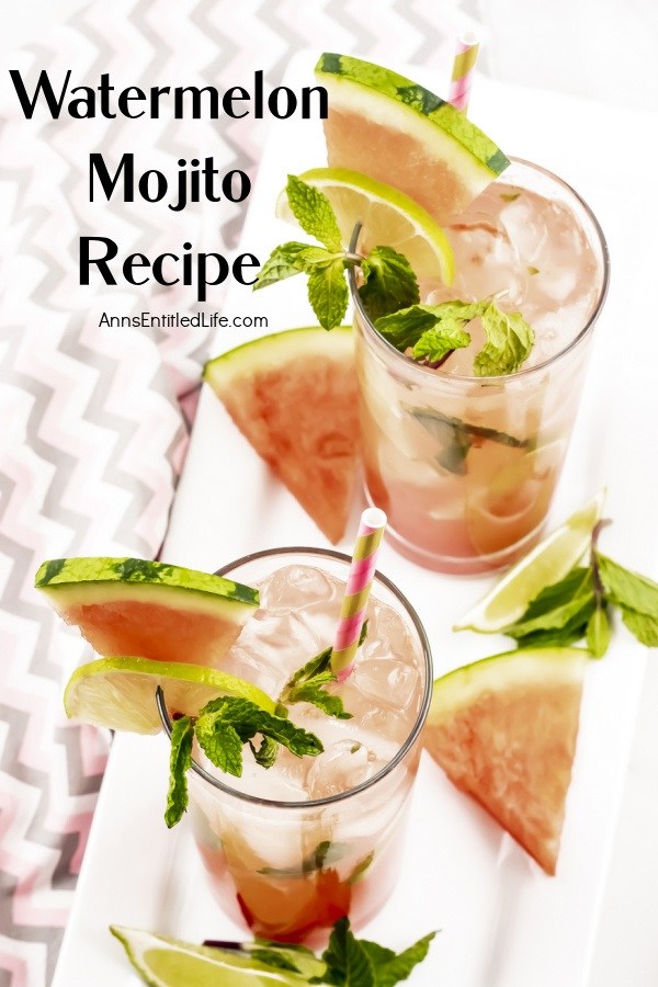 Overhead view of two watermelon mojitos on a white tray surrounded by cut watermelon, lime slices, and min springs. This sits on a pink and grey chevron napkin.