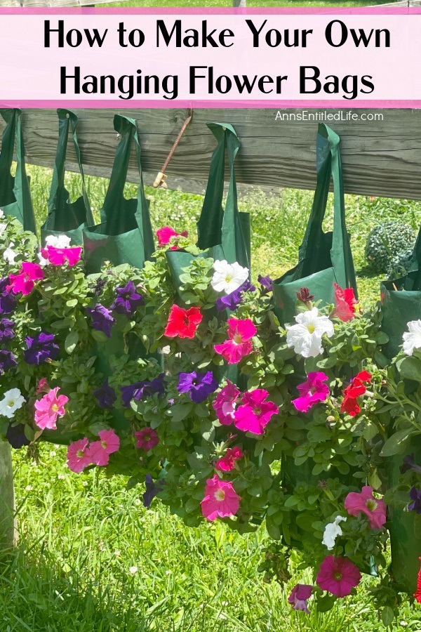 Six hanging flower pouches filled with red, white, and purple petunias hanging on nails on a wooden fence