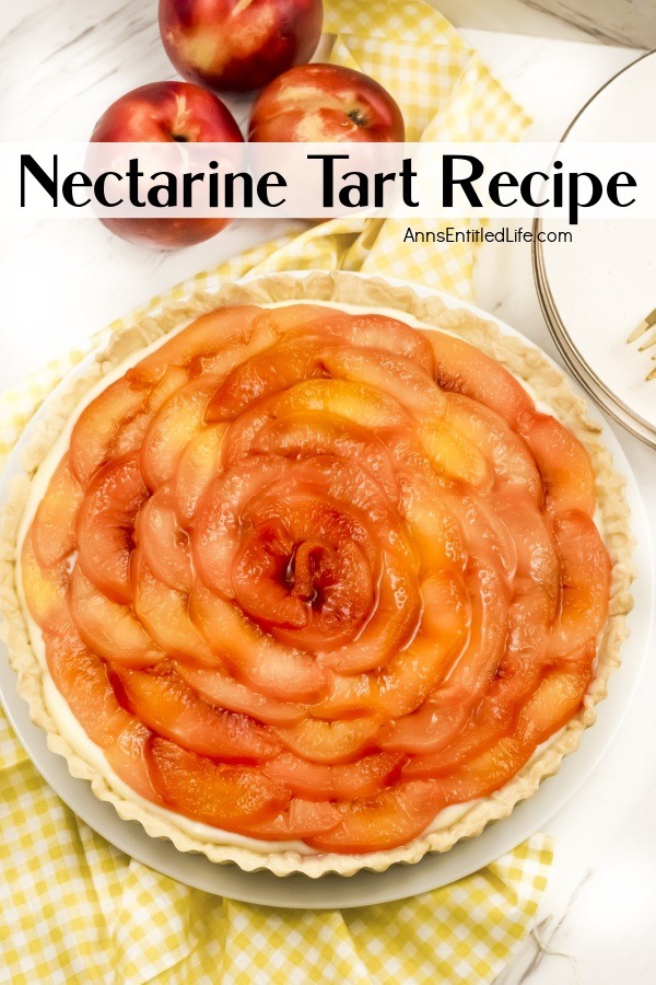 Overhead view of a nectarine tart on a white and yellow checked cloth. There are fresh nectarines above the tart, and a partial view of white plates on the right.