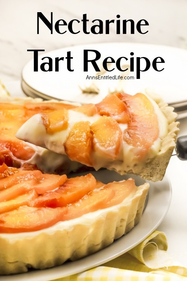 A piece of a nectarine tart is being lifted from the tart below. There are white plates and gold forks above the tart.