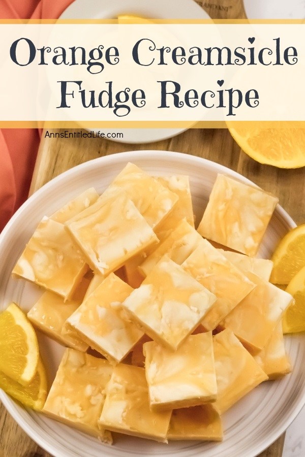 An overhead photo of a white plate filled with cut squares of orange creamsicle fudge. There are orange slice garnishes surrounding the fudge.