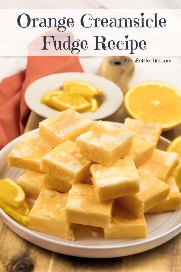 A side view of a white plate filled with cut squares of orange creamsicle fudge. There are orange slice garnishes surrounding the fudge.