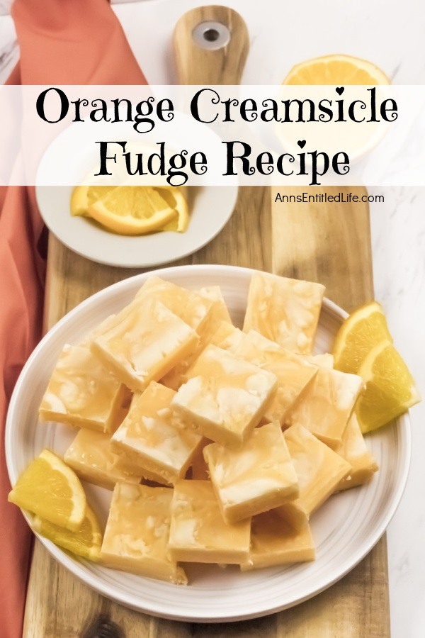 An overhead photo of a white plate filled with cut squares of orange creamsicle fudge. There are orange slice garnishes surrounding the fudge, as well as a small white bowl filled with orange slices above the plate.